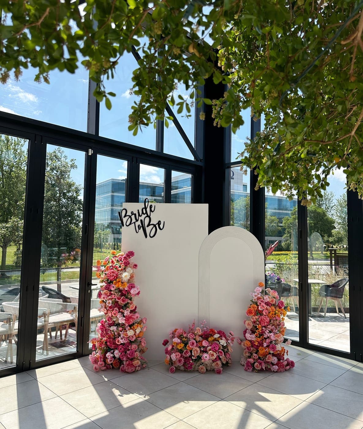 Bridal shower arch floral backdrop rental Chicago — Bride to Be white arch with lush pink orange floral arrangements